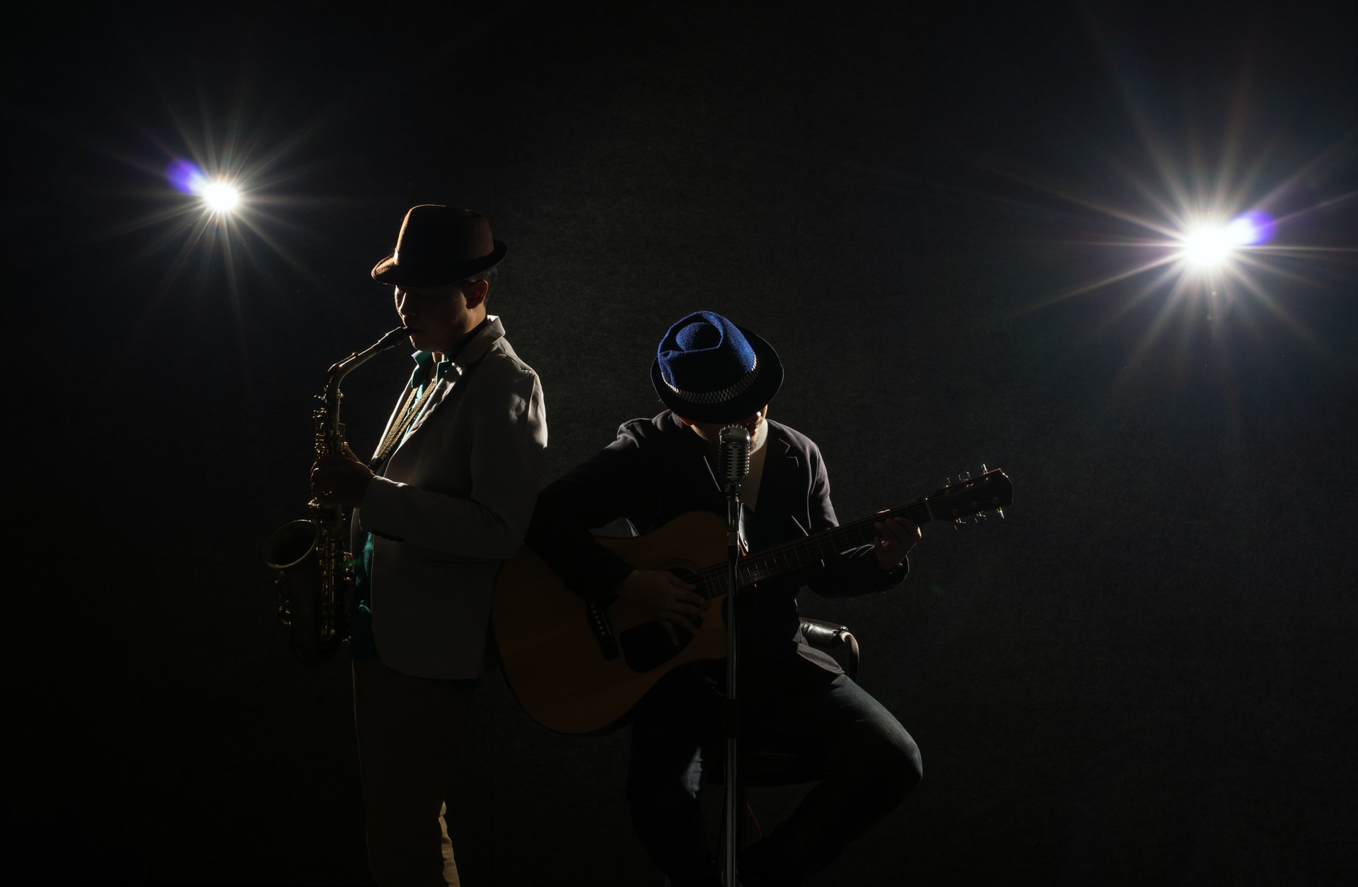 Musician Duo band playing a saxophone and singing a song and playing the guitar on black background with spot light and lens flare, musical concept